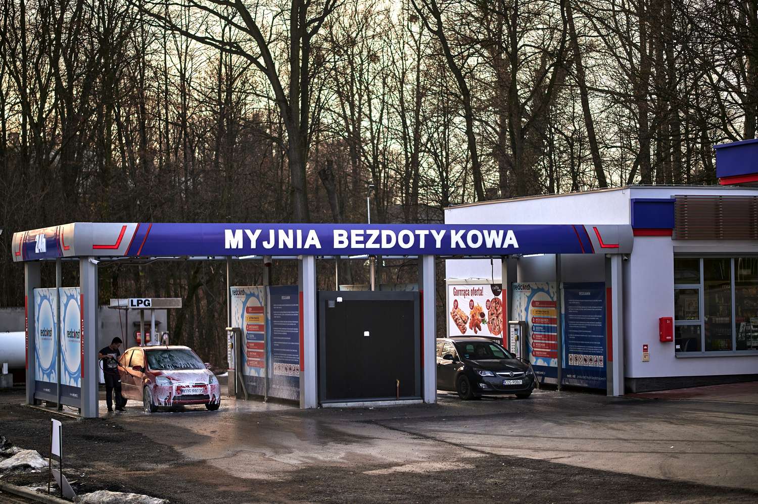 Myjnia bezdotykowa z widokiem na samochód poddaną myciu. W tle widać stację LPG oraz reklamy usług. Idealne miejsce dla miłośników czystych samochodów.