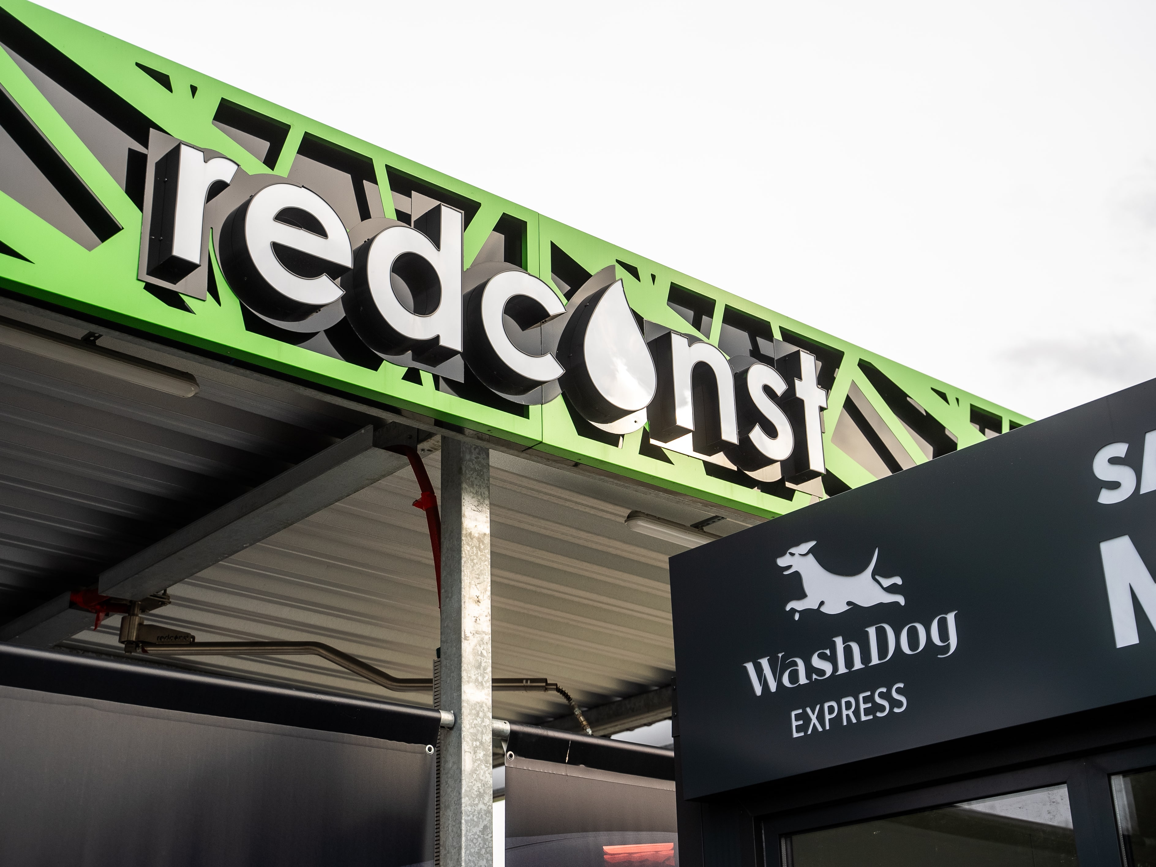 Widok na znak producenta myjni bezdotykowej "redconst" oraz logo "WashDog Express", podkreślający nowoczesne usługi myjni. Idealne dla osób szukających innowacyjnych rozwiązań w zakresie mycia pojazdów.